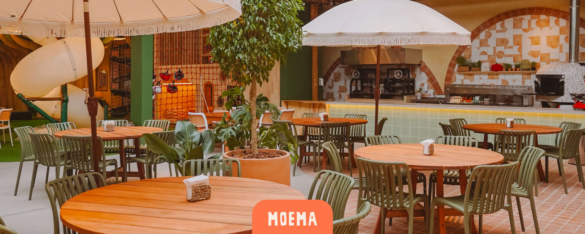 Cachola Moema - salão de refeições com mesas redondas de madeira, cadeiras verdes e guarda-sóis com franjas