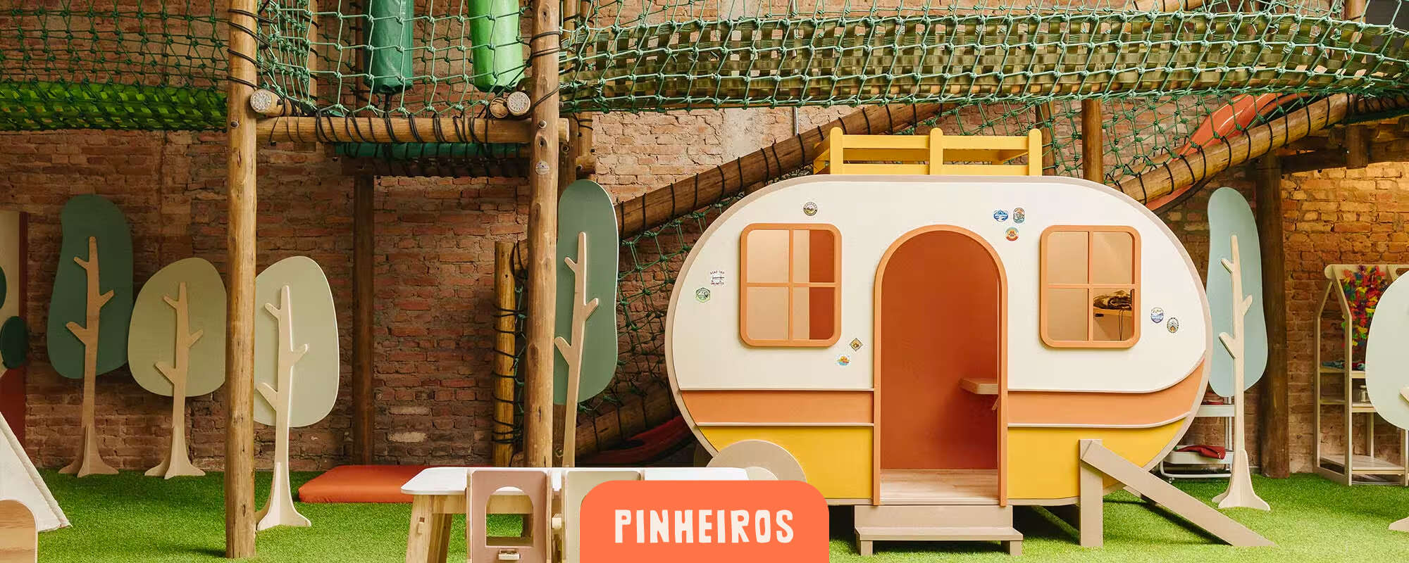 Cachola Pinheiros - área kids com trailer de brinquedo, mesinha infantil e rede de escalada sobre grama sintética