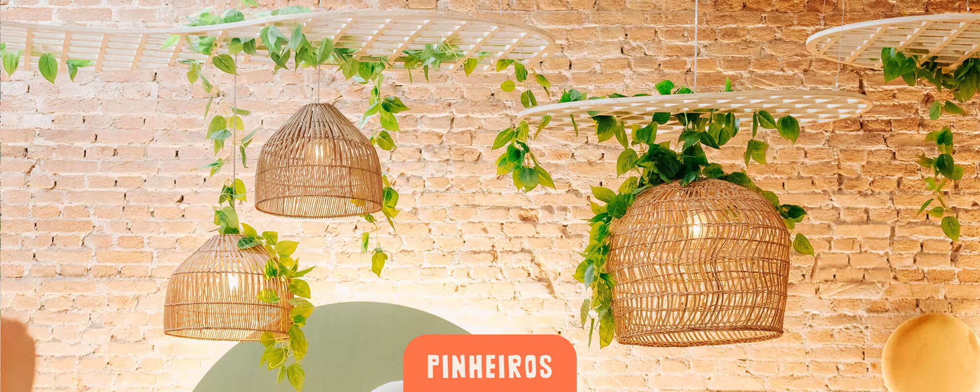 Cachola Pinheiros - detalhe de luminárias de rattan com folhagens sobre parede de tijolo aparente